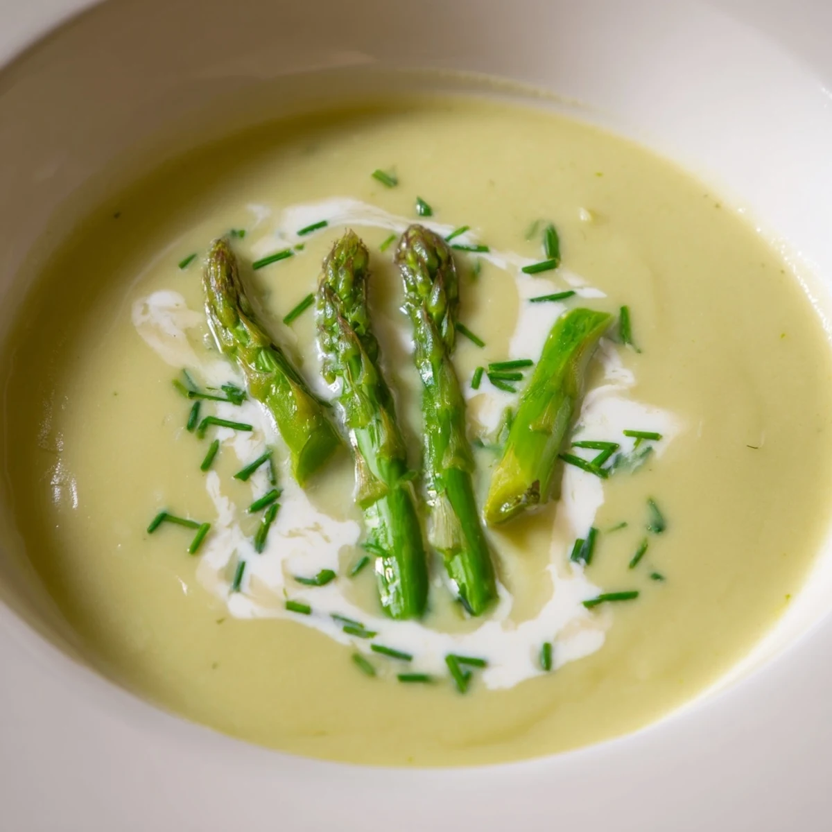 Smooth green asparagus soup with lemon zest, served hot in a white bowl with blanched tips and herbs.