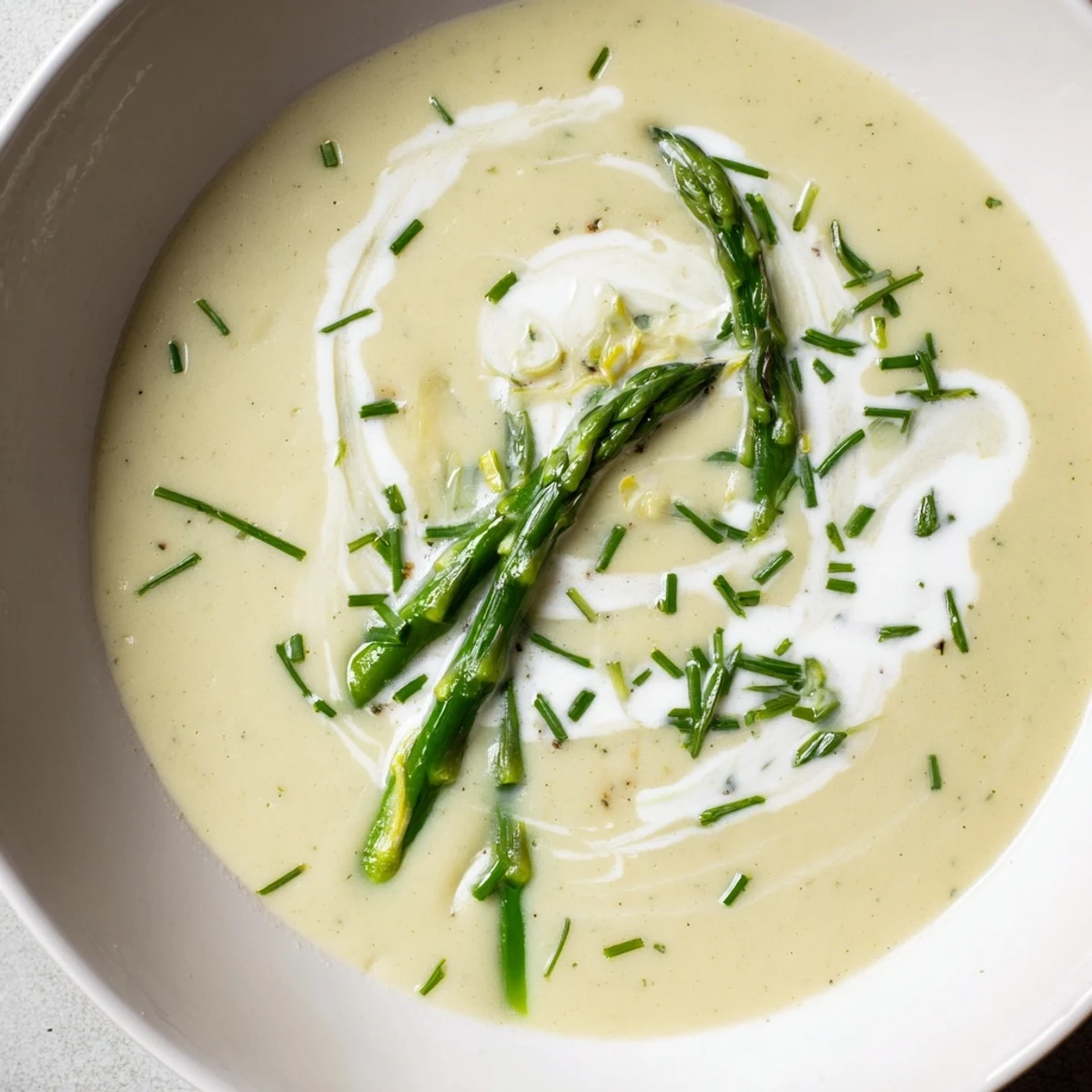 Creamy asparagus soup with lemon, garnished with fresh chives and a swirl of cream for a bright, spring-inspired appetizer.