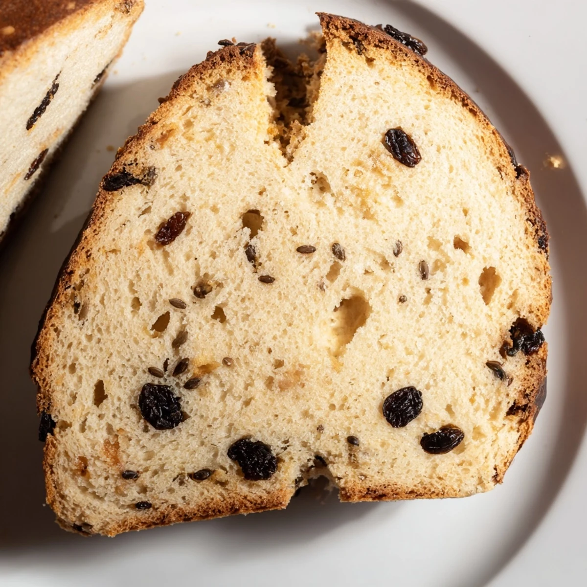 Freshly baked Irish Soda Bread with Currants and Caraway, sliced to show its tender, airy crumb studded with dark fruit and aromatic seeds, ready to be enjoyed with a cup of tea.  
