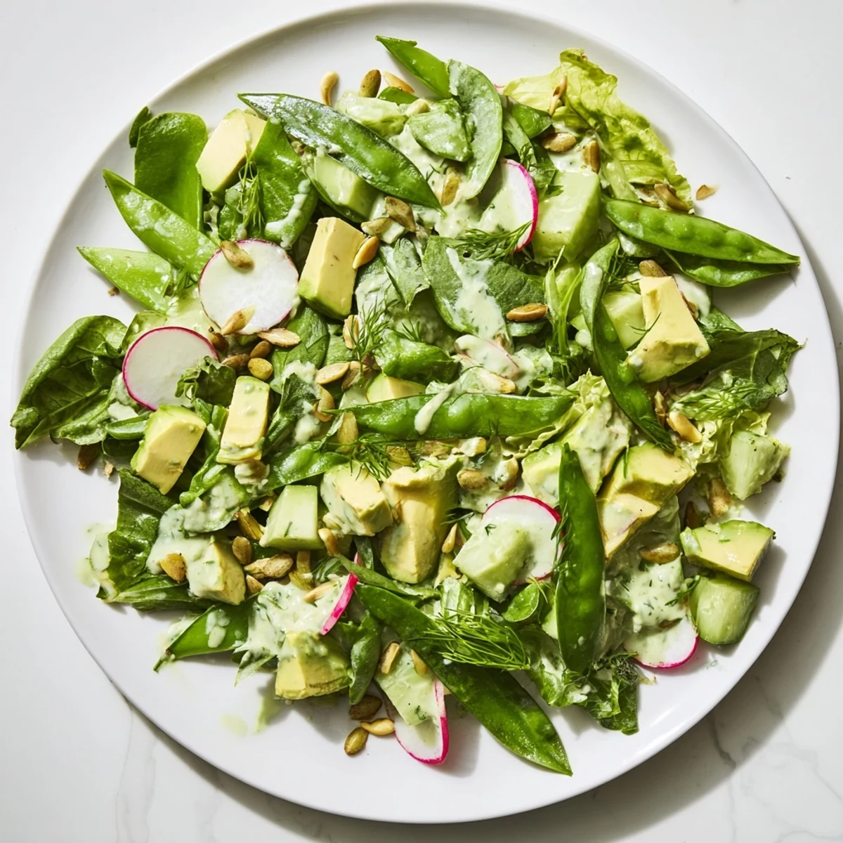A close-up of a vibrant Green Goddess Salad with avocado, cucumber, and radishes in a rustic white bowl.