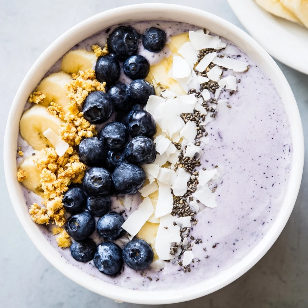 Brightly colored Lemon Blueberry Smoothie Bowl topped with granola, fresh berries, and sliced almonds in a ceramic bowl.