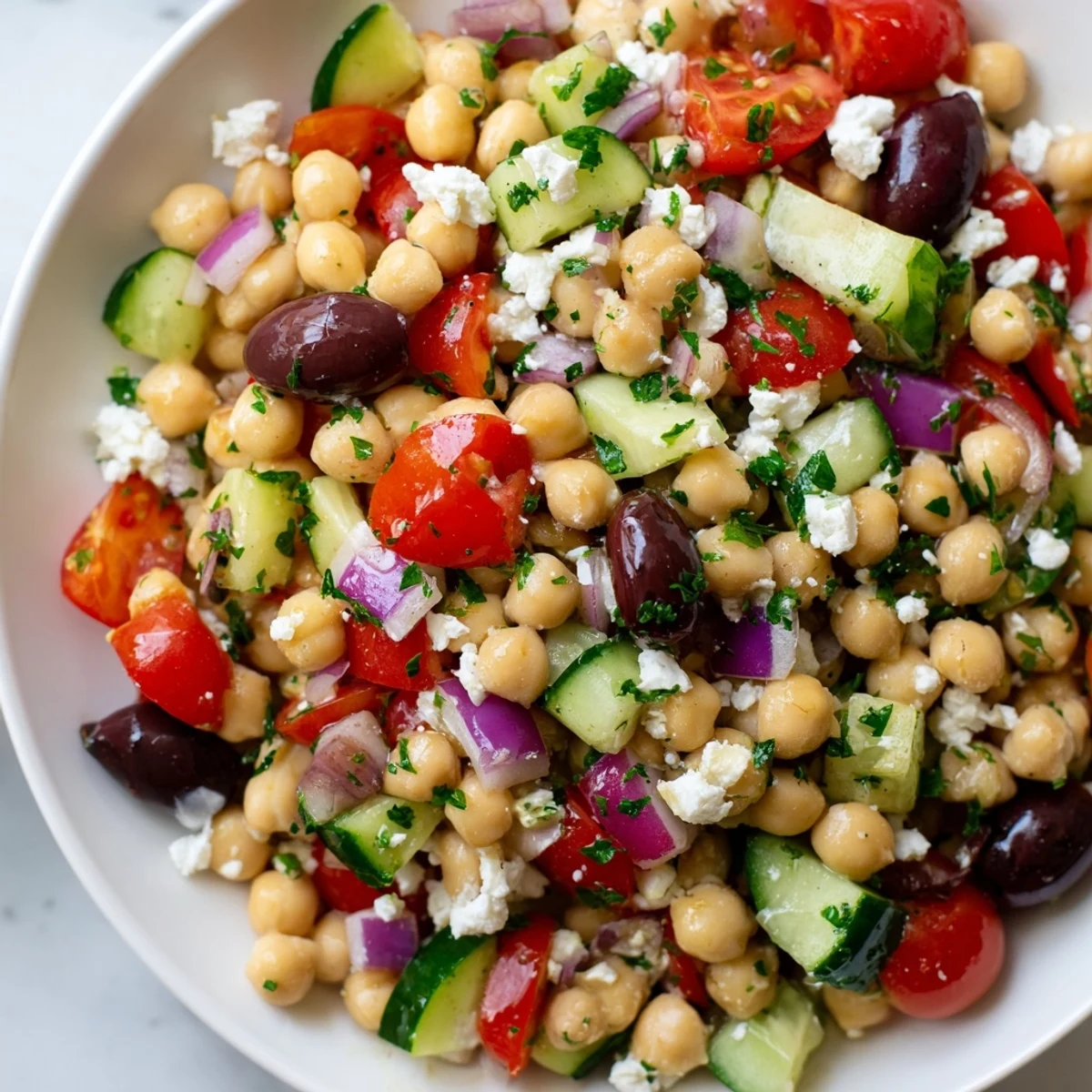 Mediterranean Chickpea Salad with Feta in a ceramic bowl, showcasing vibrant cherry tomatoes and crisp cucumbers tossed in lemon-oregano dressing.
