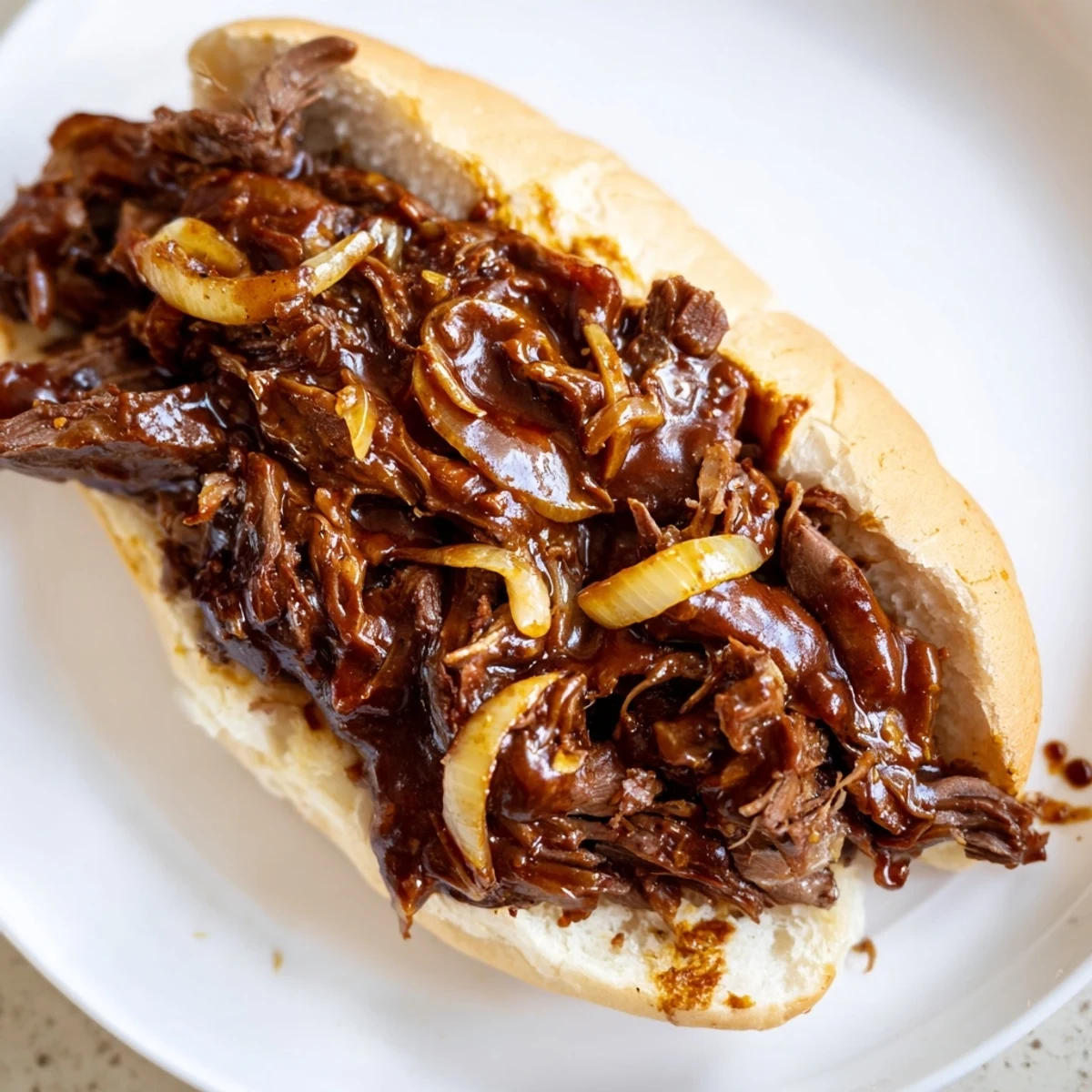 Golden-brown shredded beef piled high on a soft sandwich bun, slow-cooked and topped with tangy barbecue sauce for a crowd-pleasing meal.