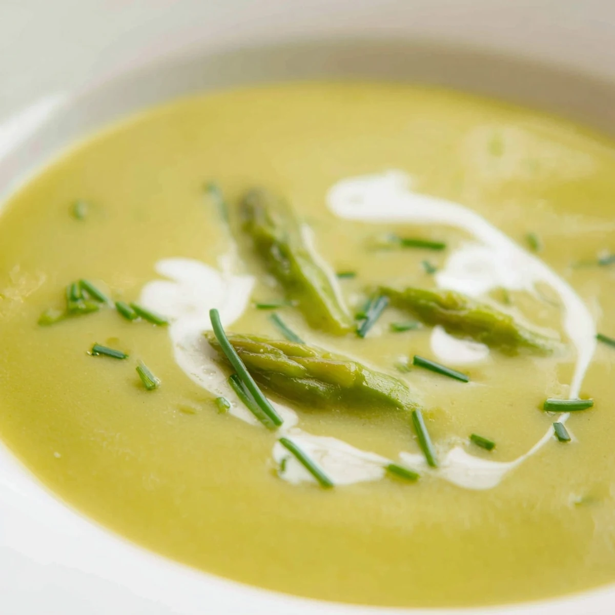 Creamy Asparagus Soup with Lemon presented in a white bowl with a swirl of cream and fresh chives, perfect for springtime meals.