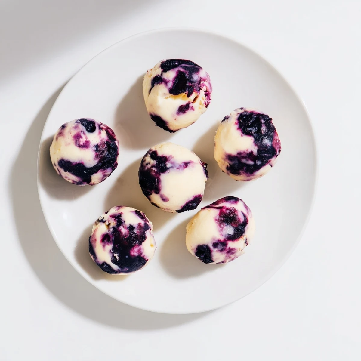These no-bake Blueberry Cheesecake Protein Bites are stacked on a white plate, showing their creamy filling and graham cracker crumbs.