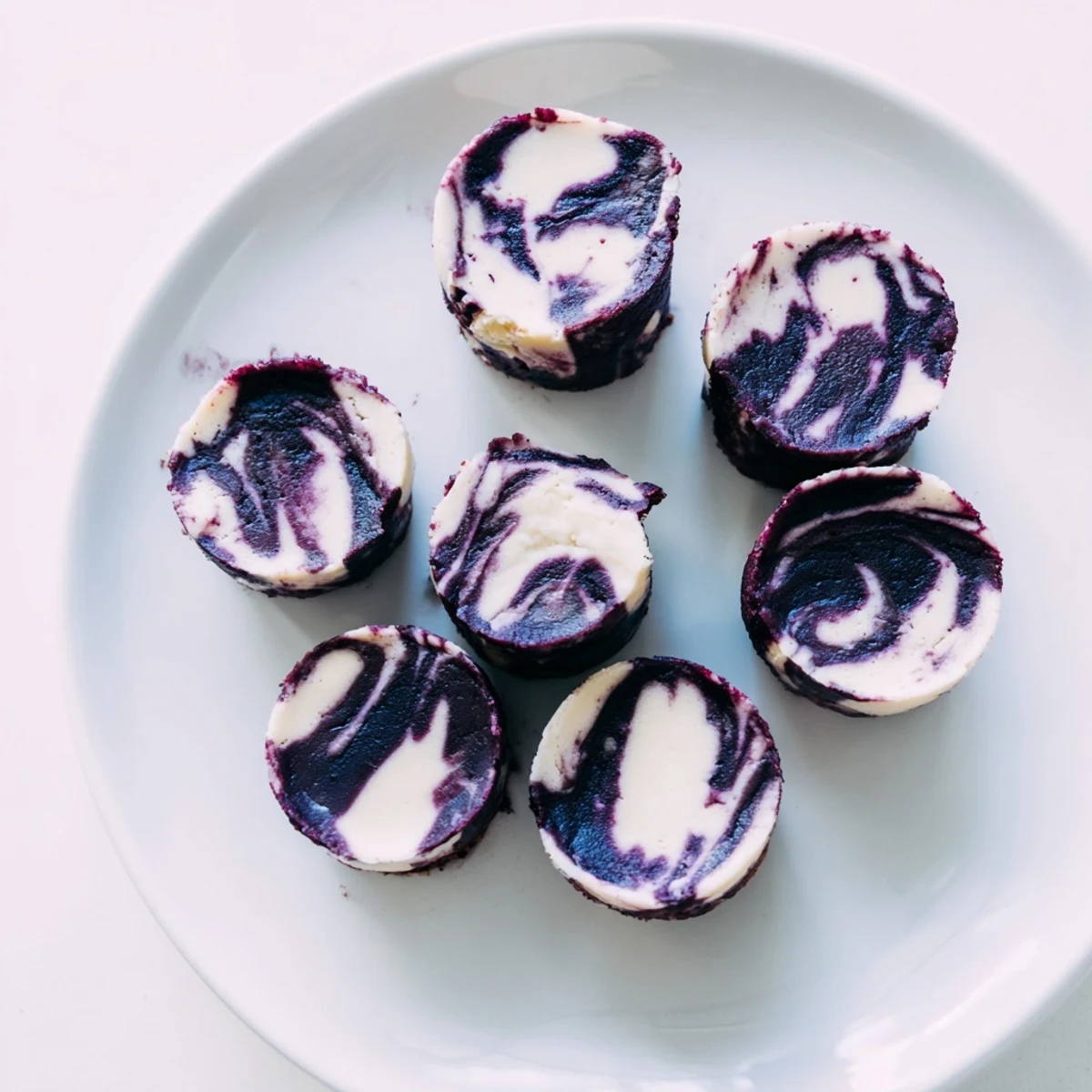 A hand holding a Blueberry Cheesecake Protein Bite, revealing the soft texture and vibrant blueberry swirl inside.