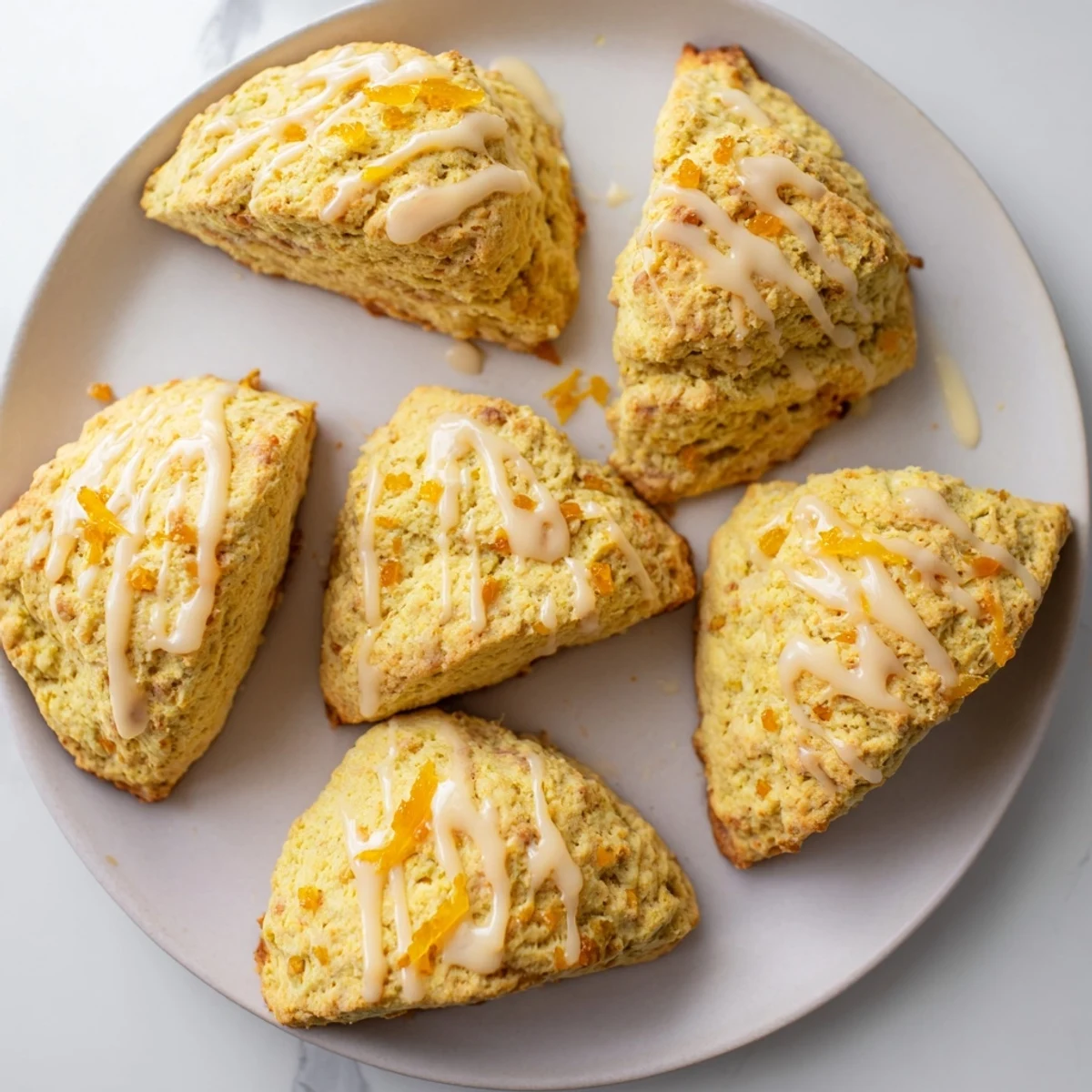 Eight golden-brown Candied Ginger Orange Scones are lined up on a baking sheet, filled with visible chunks of candied ginger.