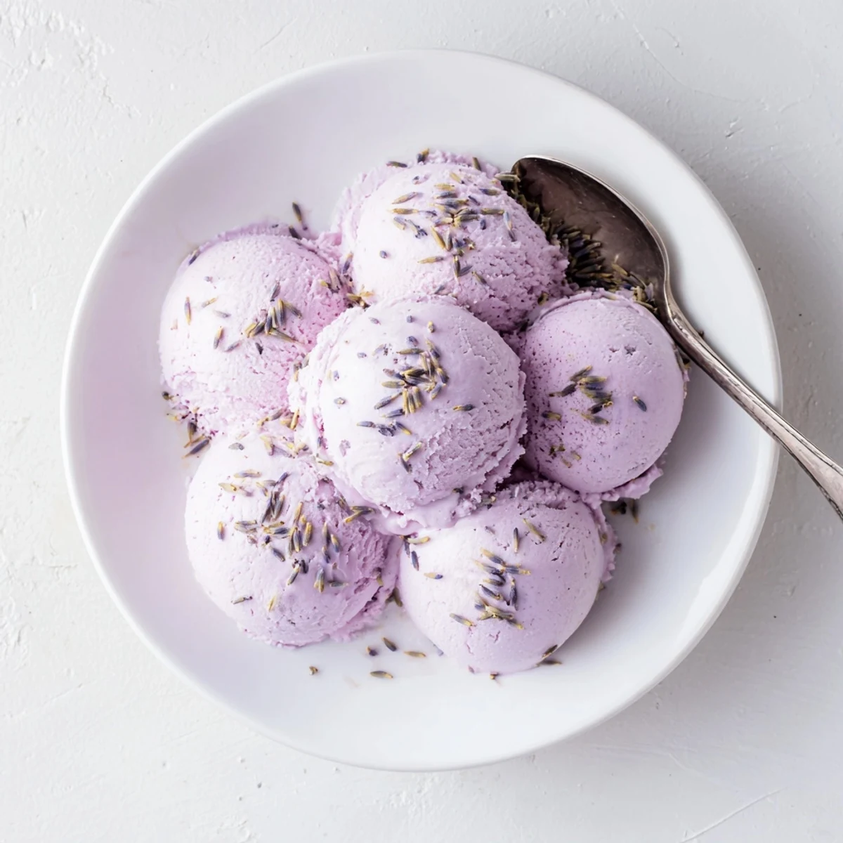 Creamy lavender ice cream in a rustic bowl, topped with purple buds and fresh berries for a refreshing summer dessert.