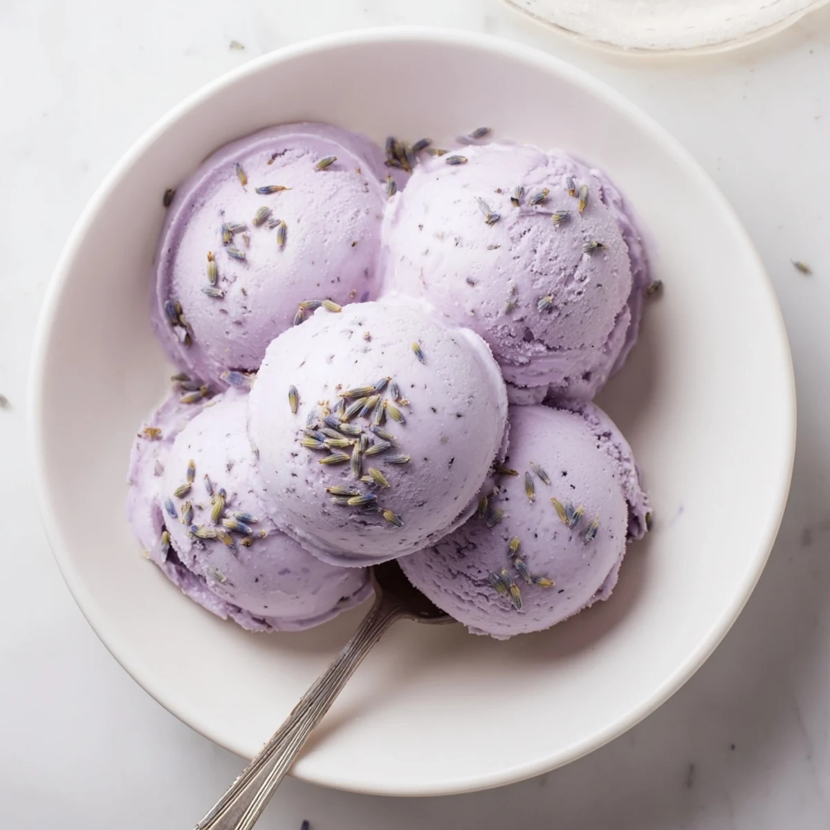 A scoop of homemade lavender ice cream in a waffle cone, dusted with powdered sugar beside a steaming cup of tea.