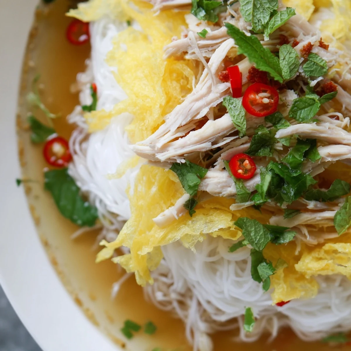 Golden egg crepe strips and shredded chicken rest on rice noodles, garnished with herbs and chilies for Bun Thang.