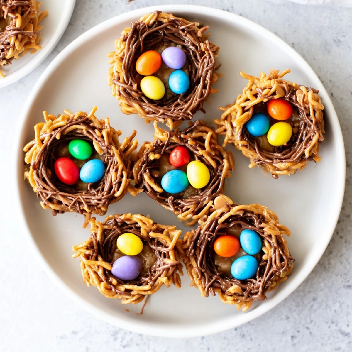 A platter of Easter Birds Nest Cookies with Peanut Butter and Chocolate arranged on pastel napkins, with bright candy eggs nestled in each chocolatey nest.