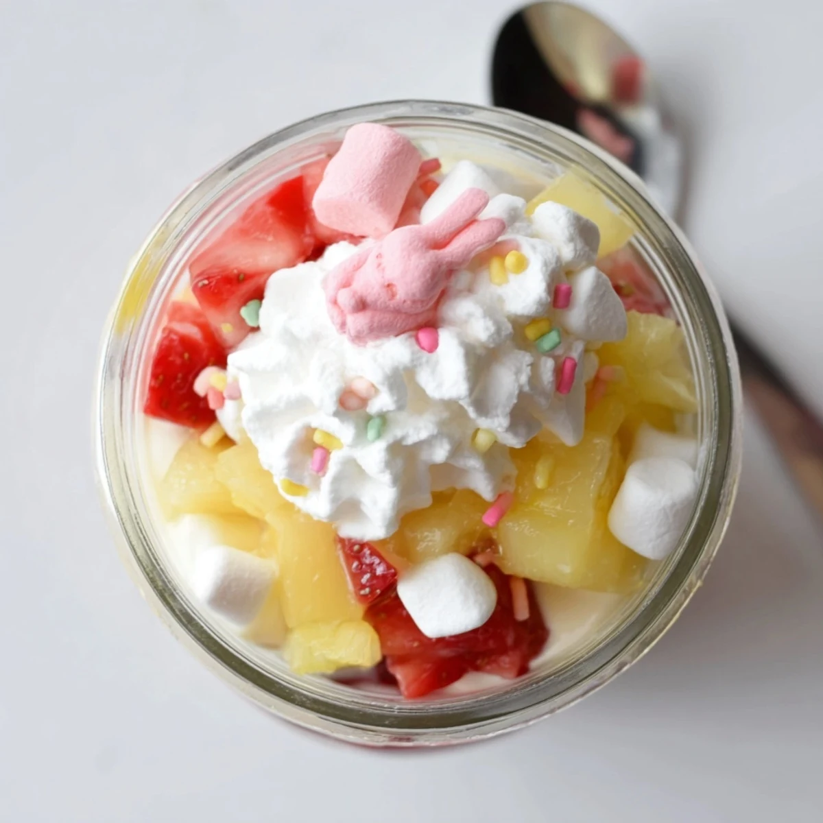 Bright layers of creamy Jello Pie Easter Bunny Parfait In A Jar with fresh strawberries, pineapple, and a pastel sprinkle finish.