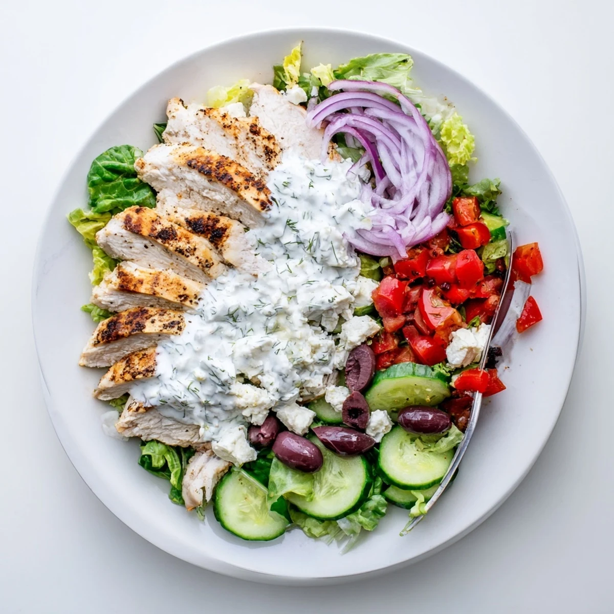 A bowl of Tzatziki Chicken Salad with olives, red onion, and cucumber, ready for a light summer lunch.