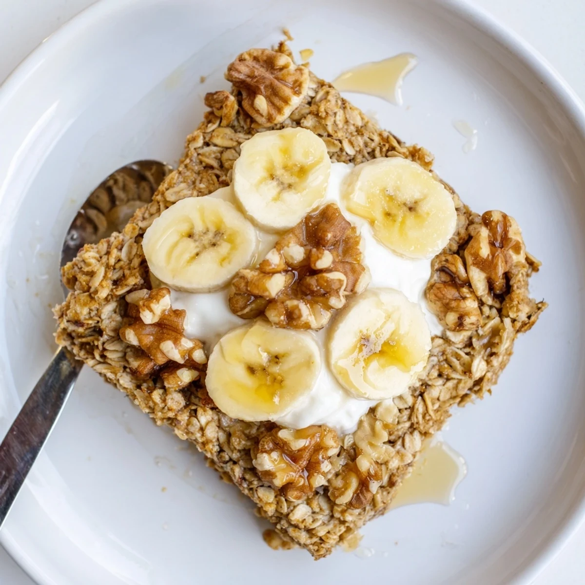 Golden-brown Banana Baked Oatmeal with Greek Yogurt topped with sliced bananas and a drizzle of maple syrup on a rustic wooden table.