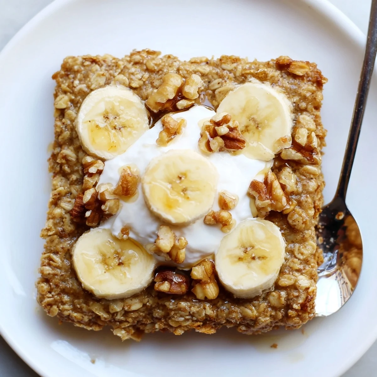 A close-up slice of Banana Baked Oatmeal with Greek Yogurt, revealing a soft texture and creamy white dollop on a white ceramic plate.