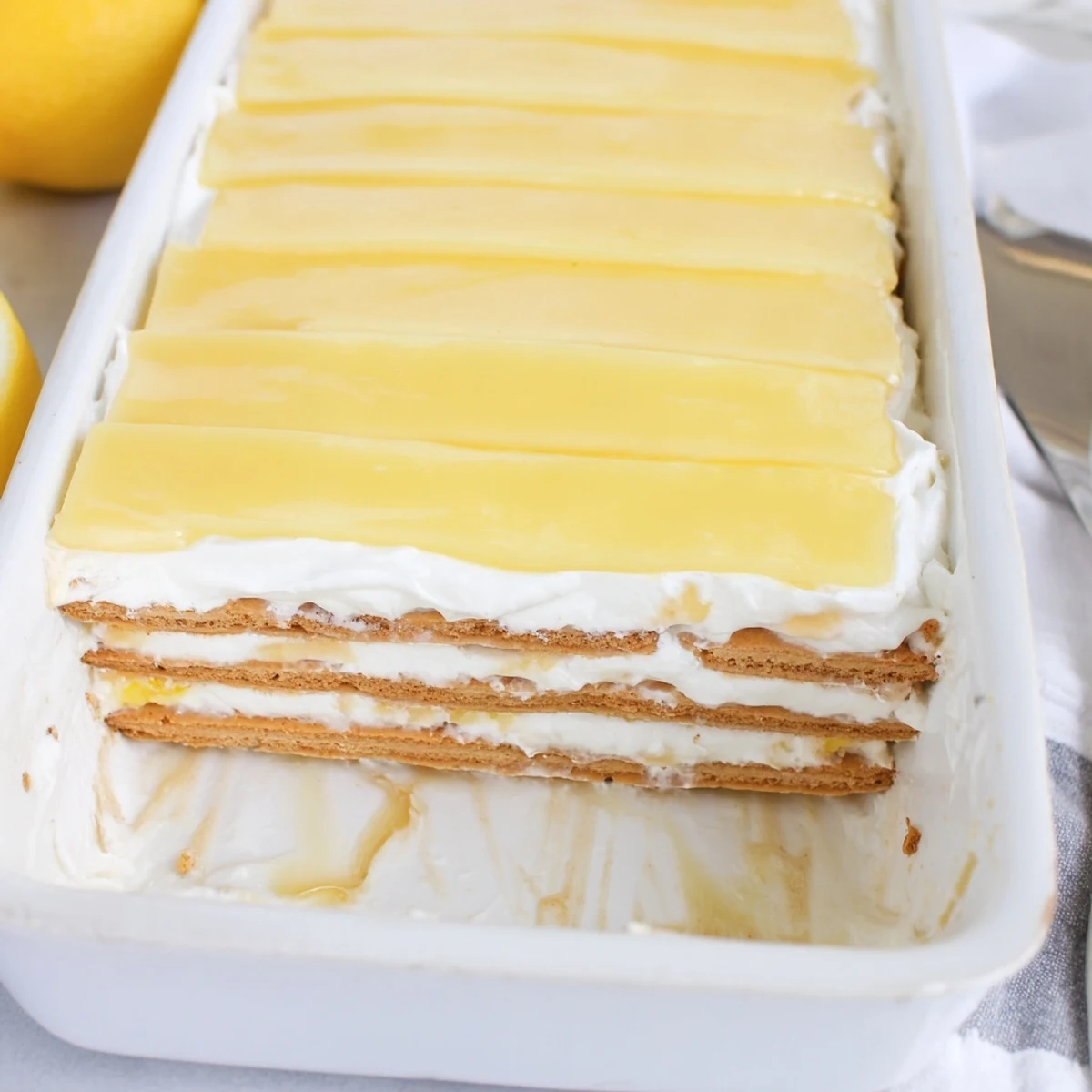 Square slice of no bake lemon eclair cake with glistening glaze and fresh lemon zest