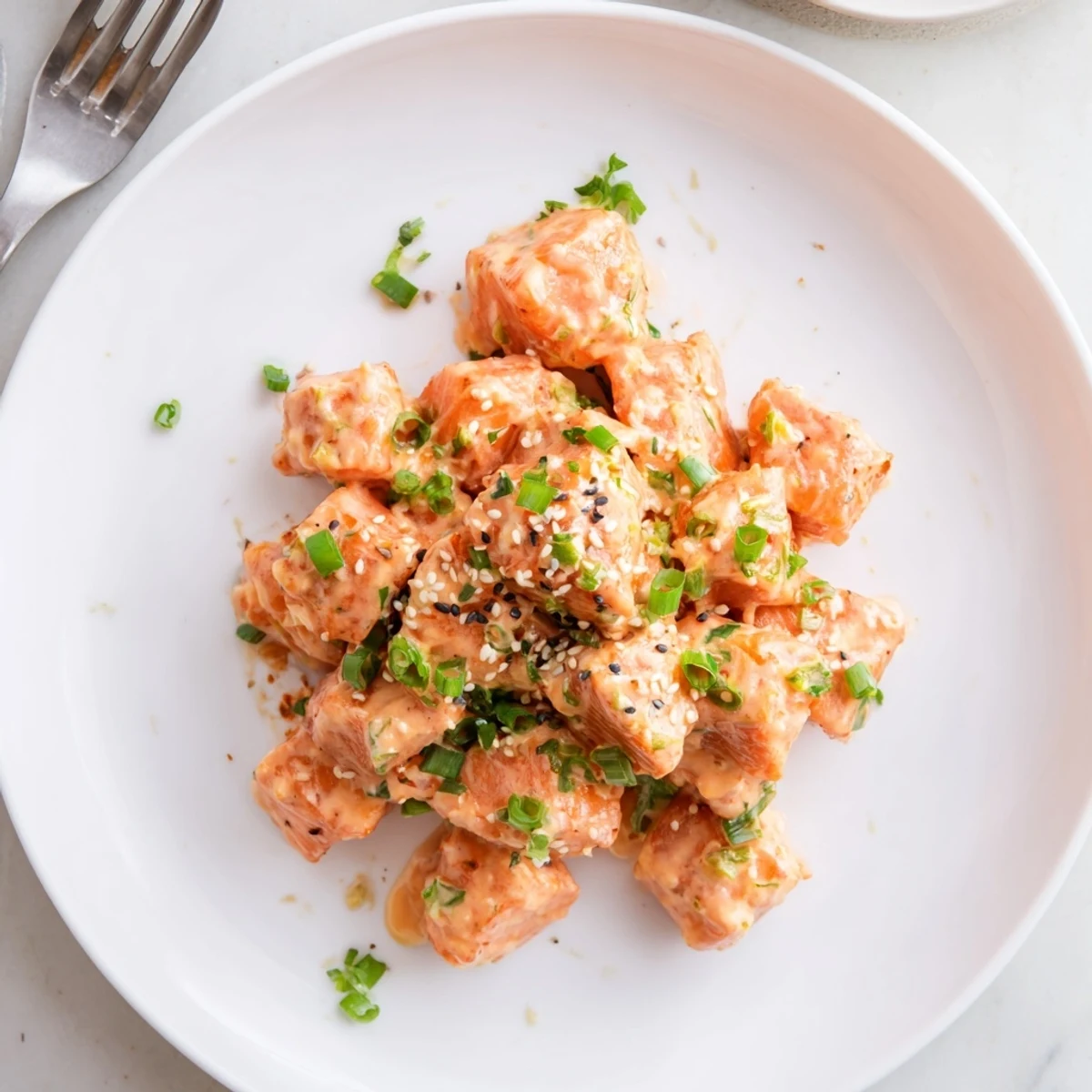 Tender fried salmon cubes tossed in sweet chili Bang Bang sauce drizzled over white serving plate