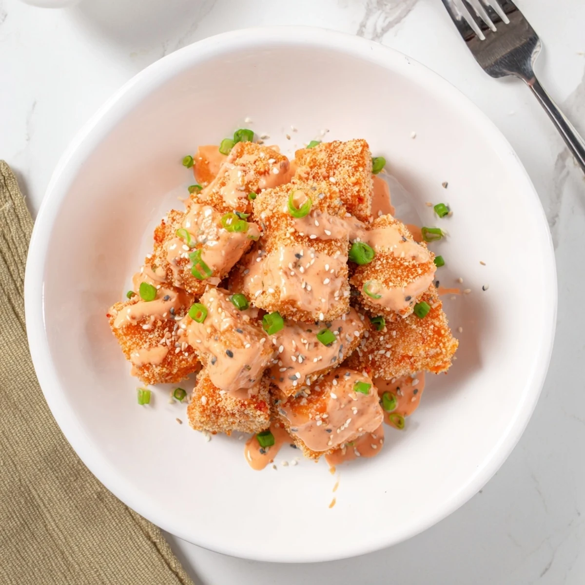 Golden crispy Bang Bang salmon bites coated in creamy spicy sauce with green onion garnish