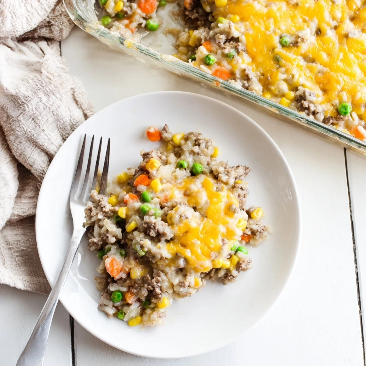 Golden cheesy ground beef and rice casserole with bubbling melted cheddar topping on a white ceramic baking dish