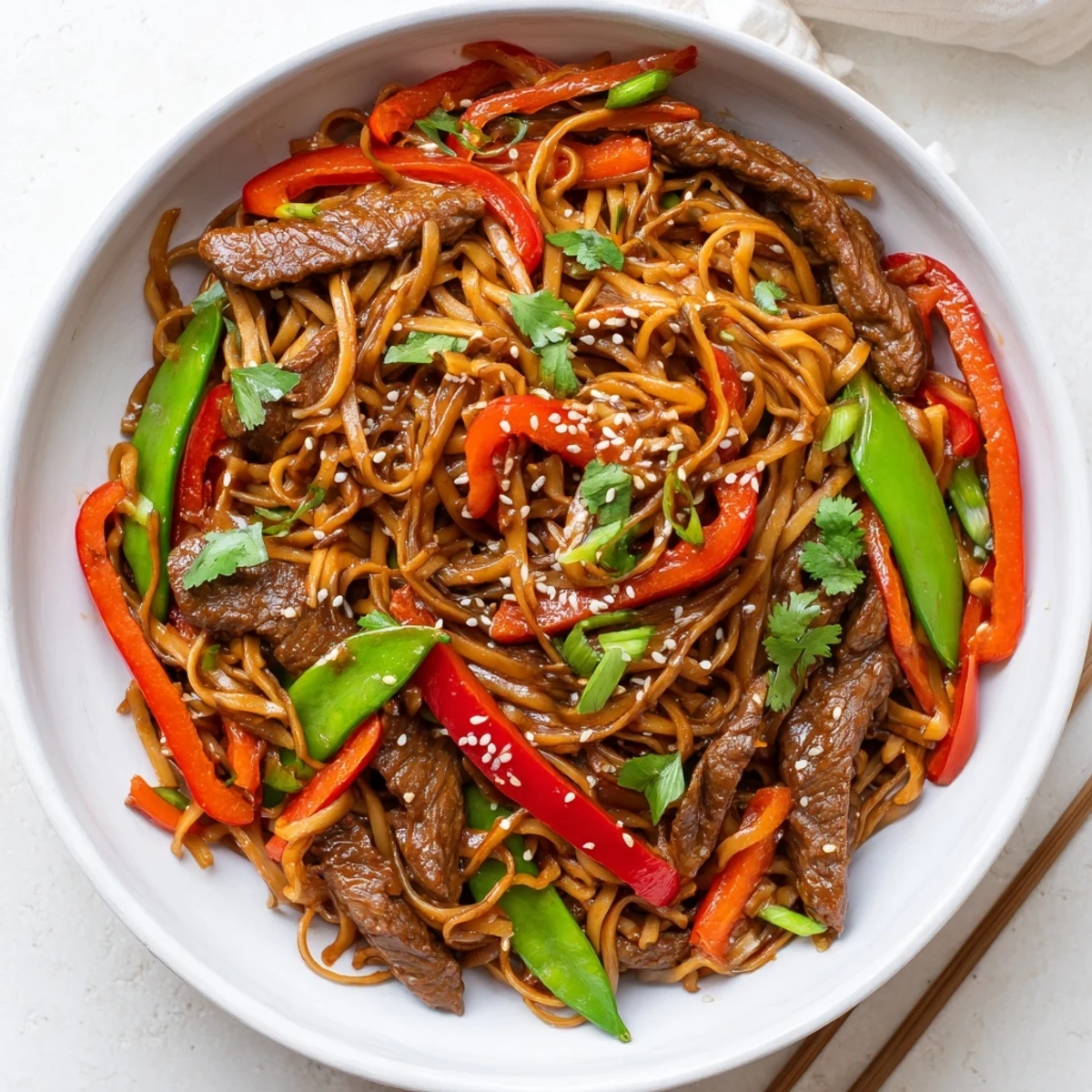 Plate of sticky beef noodles with tender meat and crisp colorful vegetables coated in glossy sauce