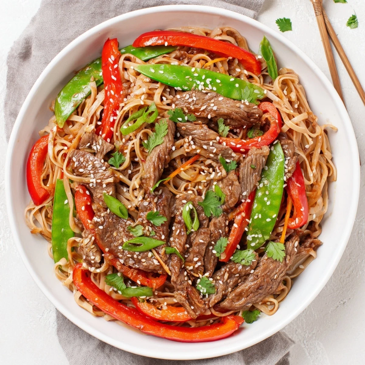 Wok-fried sticky beef noodles showcasing caramelized beef strips with bell pepper and snap pea vegetables