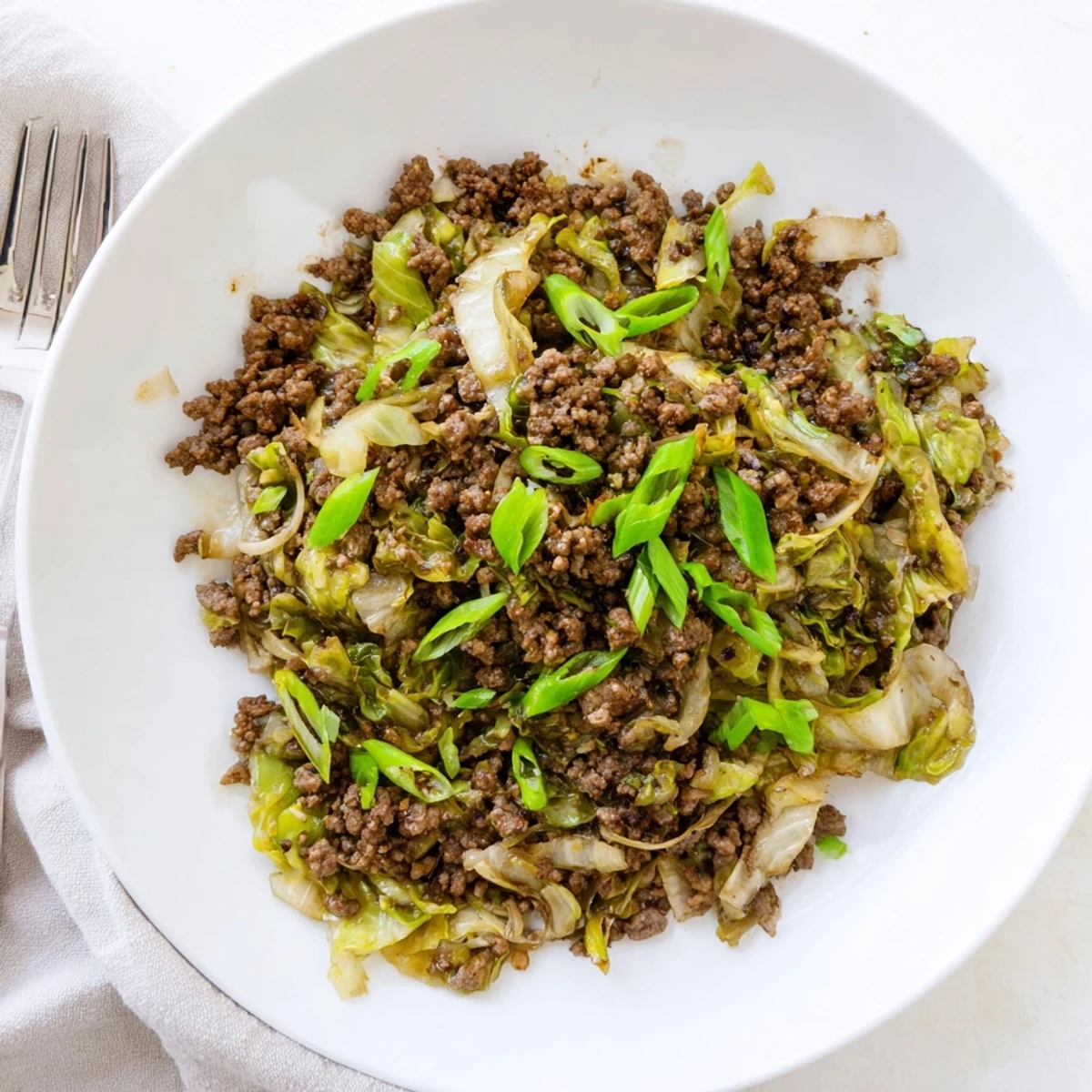 Steaming plate of Asian-inspired ground beef and cabbage with green onion garnish