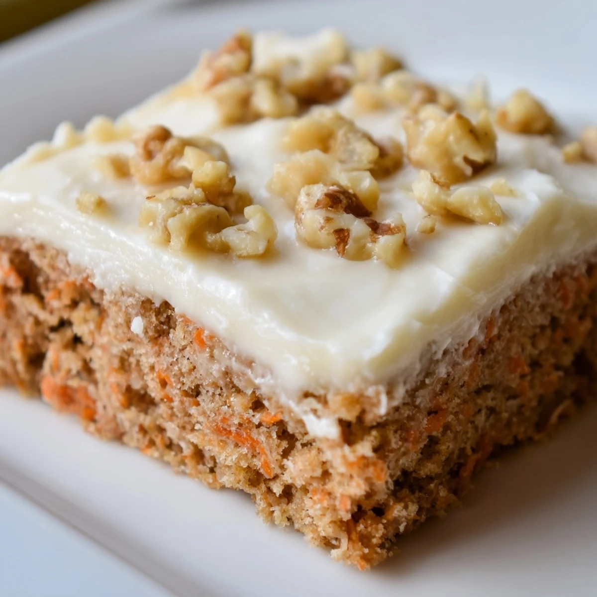 Golden carrot cake bars with spiced cake layers topped with thick cream cheese frosting and nut garnish