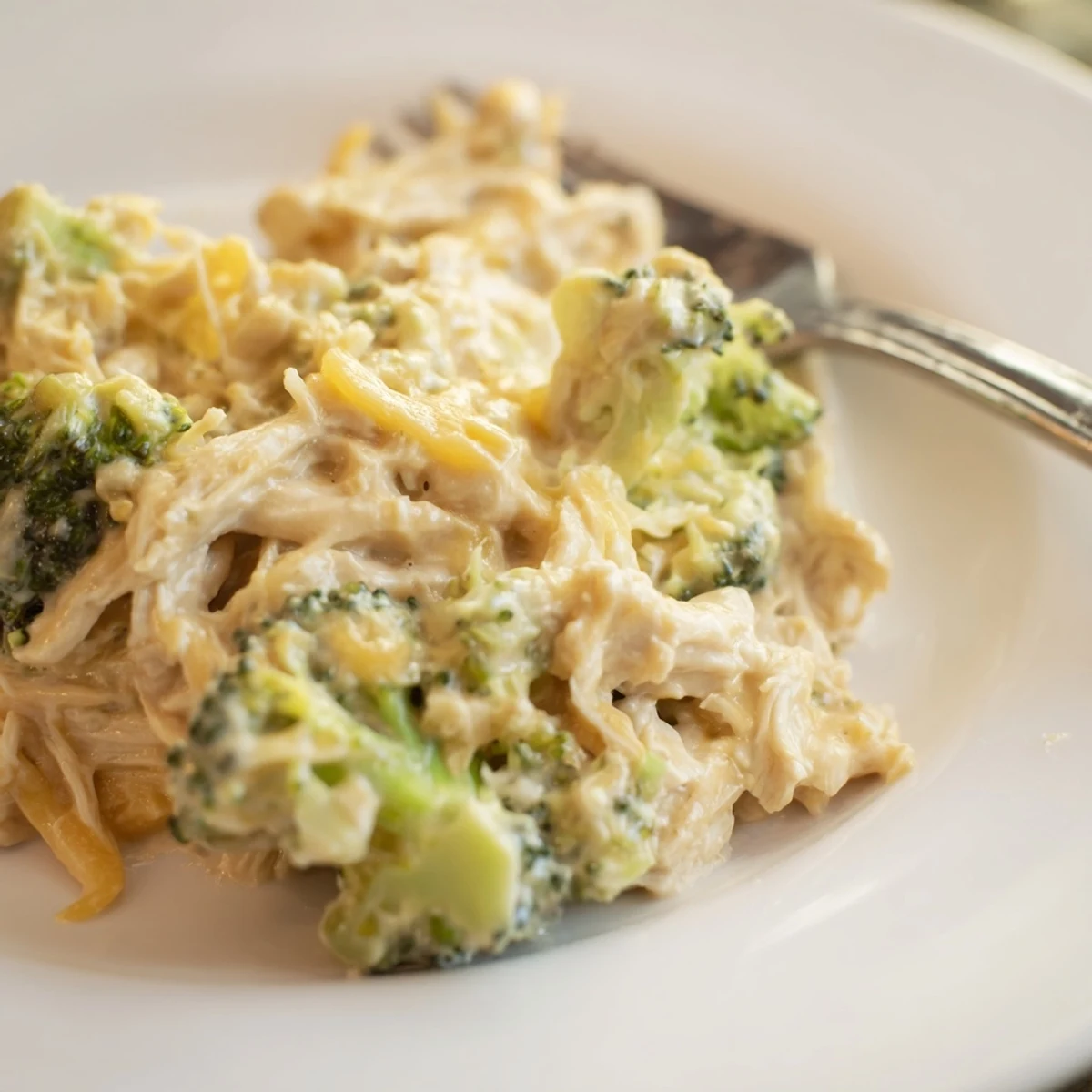 Tender slow-cooked chicken breasts in rich cheddar sauce with steamed broccoli on a rustic wooden table