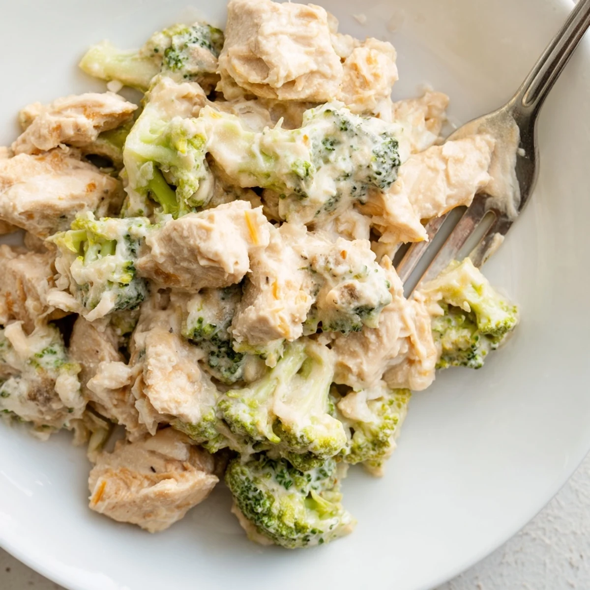 Creamy Crockpot broccoli cheddar chicken served in a white bowl with fresh green broccoli florets visible