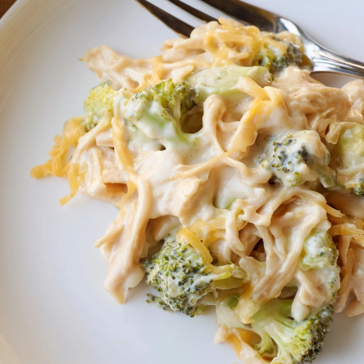 Golden shredded cheese melting over Crockpot broccoli cheddar chicken in a serving dish with dinner fork
