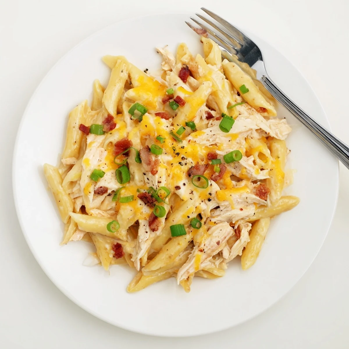 Close-up of crack chicken pasta showcasing thick Alfredo-style sauce, shredded cheddar, diced chicken breast, and savory crispy bacon topping