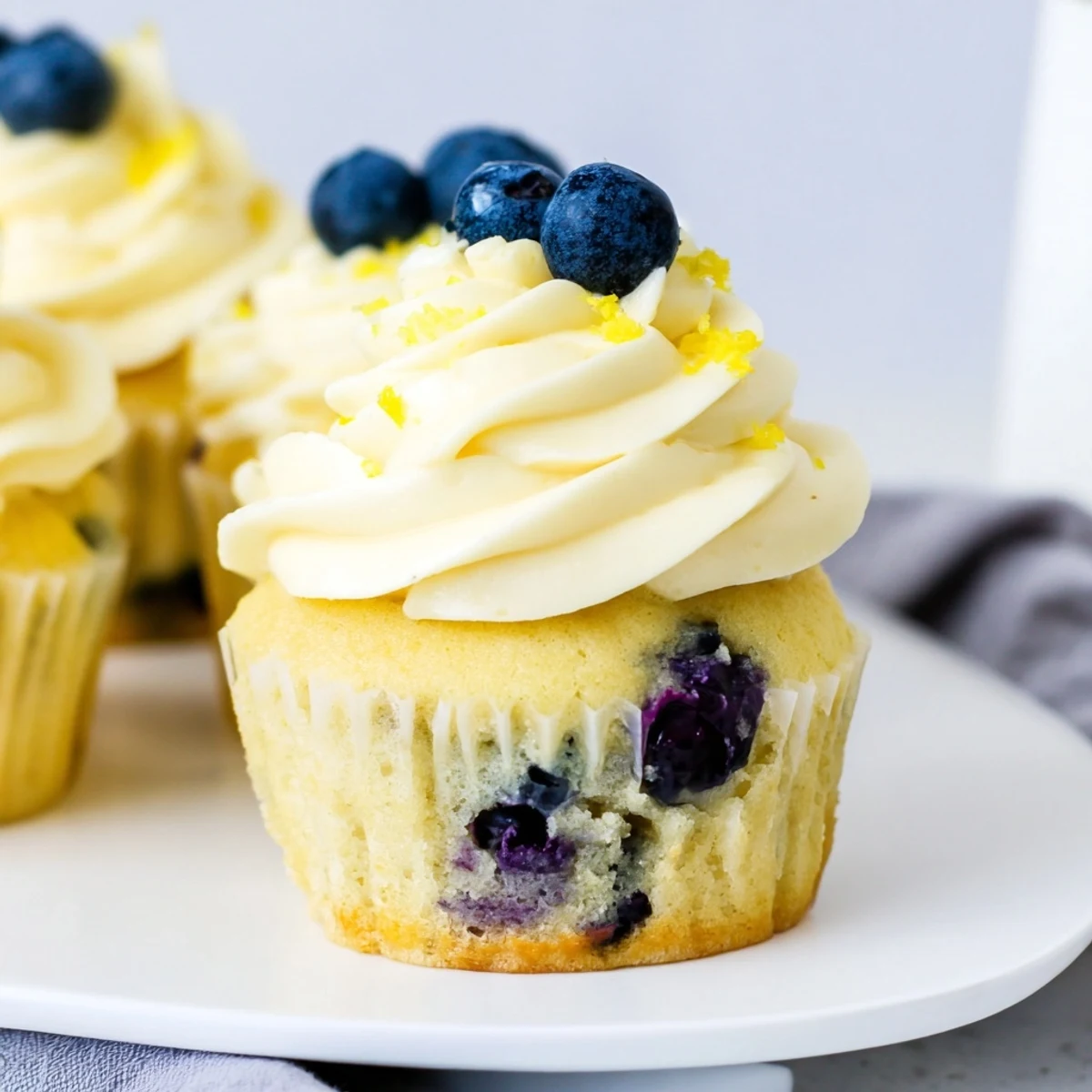 Golden lemon blueberry cupcakes with tangy cream cheese frosting garnished with zest and blueberries