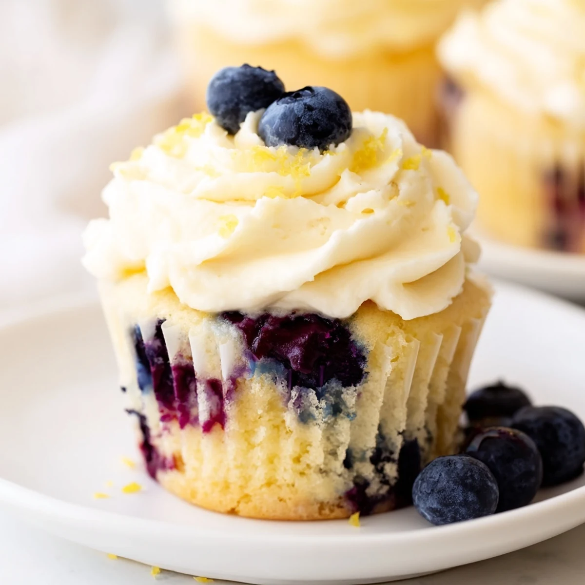 Fluffy lemon blueberry cupcakes topped with creamy lemon frosting and fresh berries on a white plate