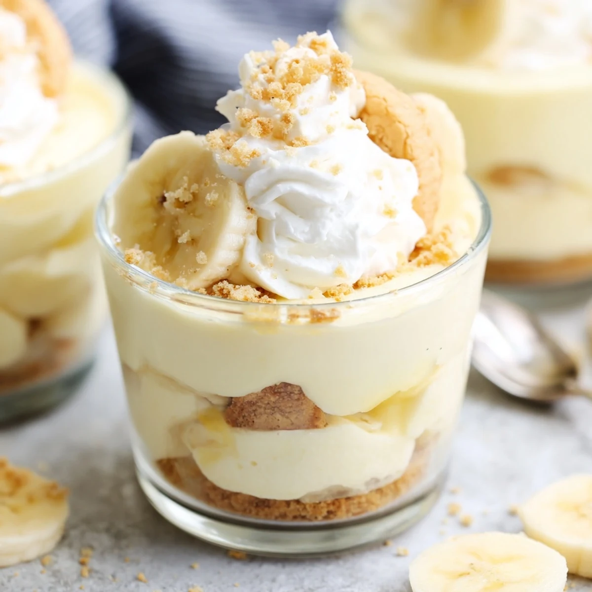 Creamy no bake banana pudding cheesecake cups topped with fresh banana slices and crunchy vanilla wafer crumbs