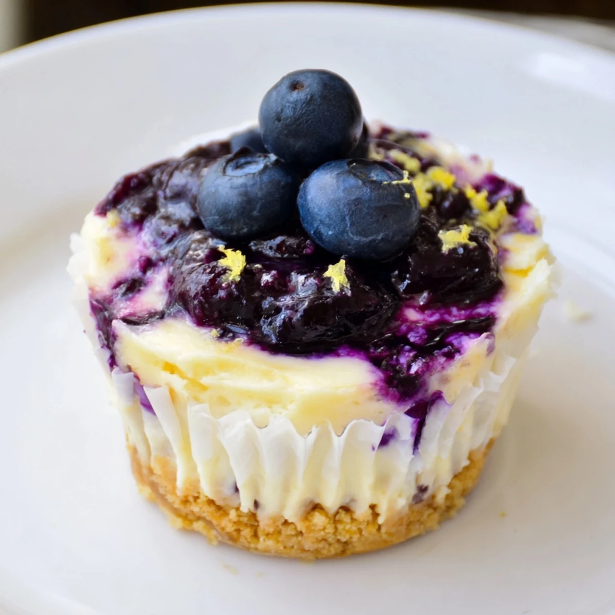 Mini lemon blueberry cheesecakes topped with glossy purple compote on a rustic baking tray