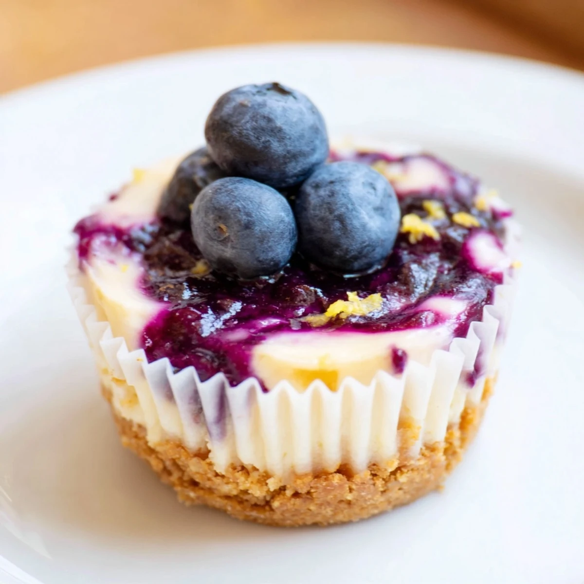 Creamy mini lemon blueberry cheesecakes with buttery graham crusts swirled with vibrant berry sauce