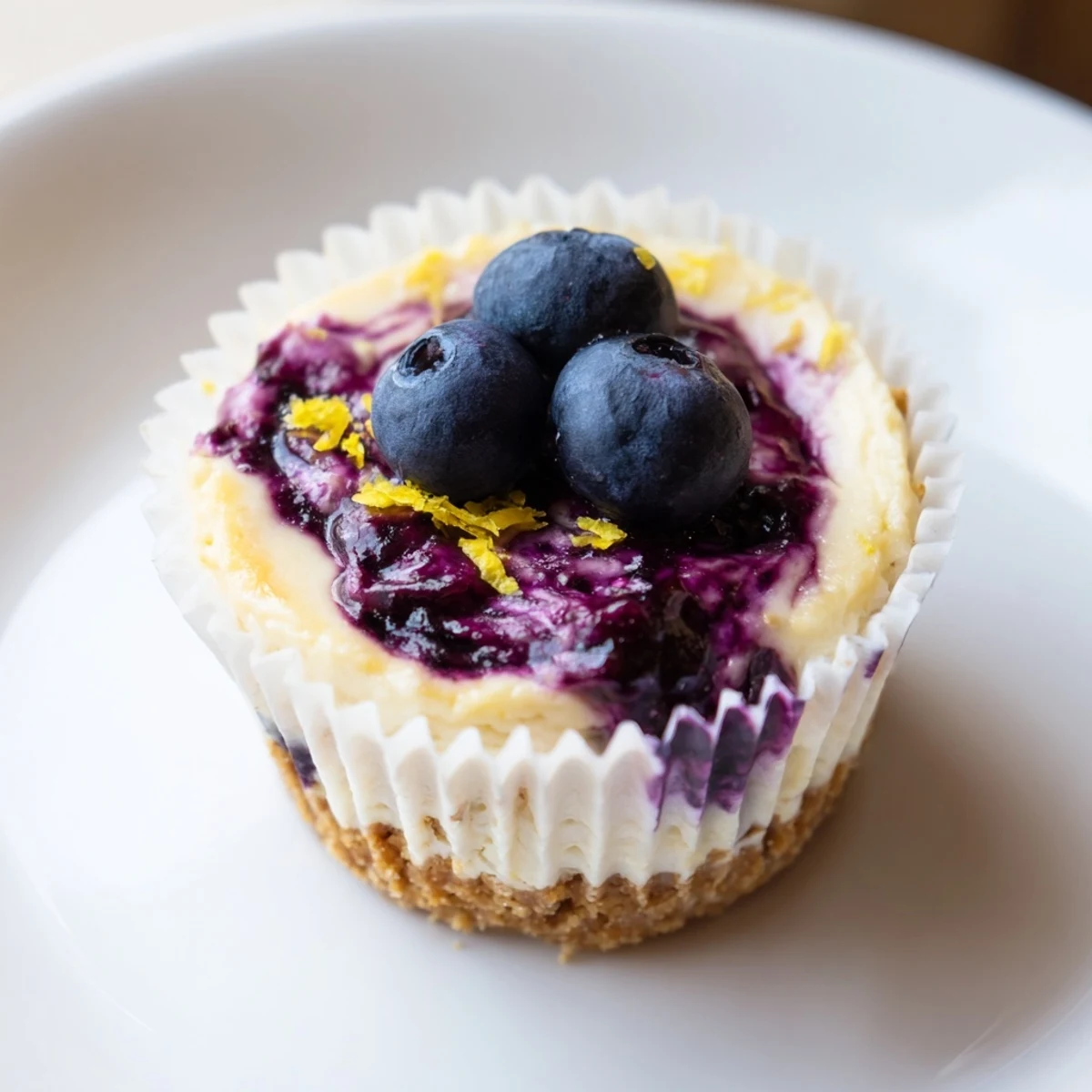 Individual mini lemon blueberry cheesecakes garnished with fresh berries and bright lemon zest curls