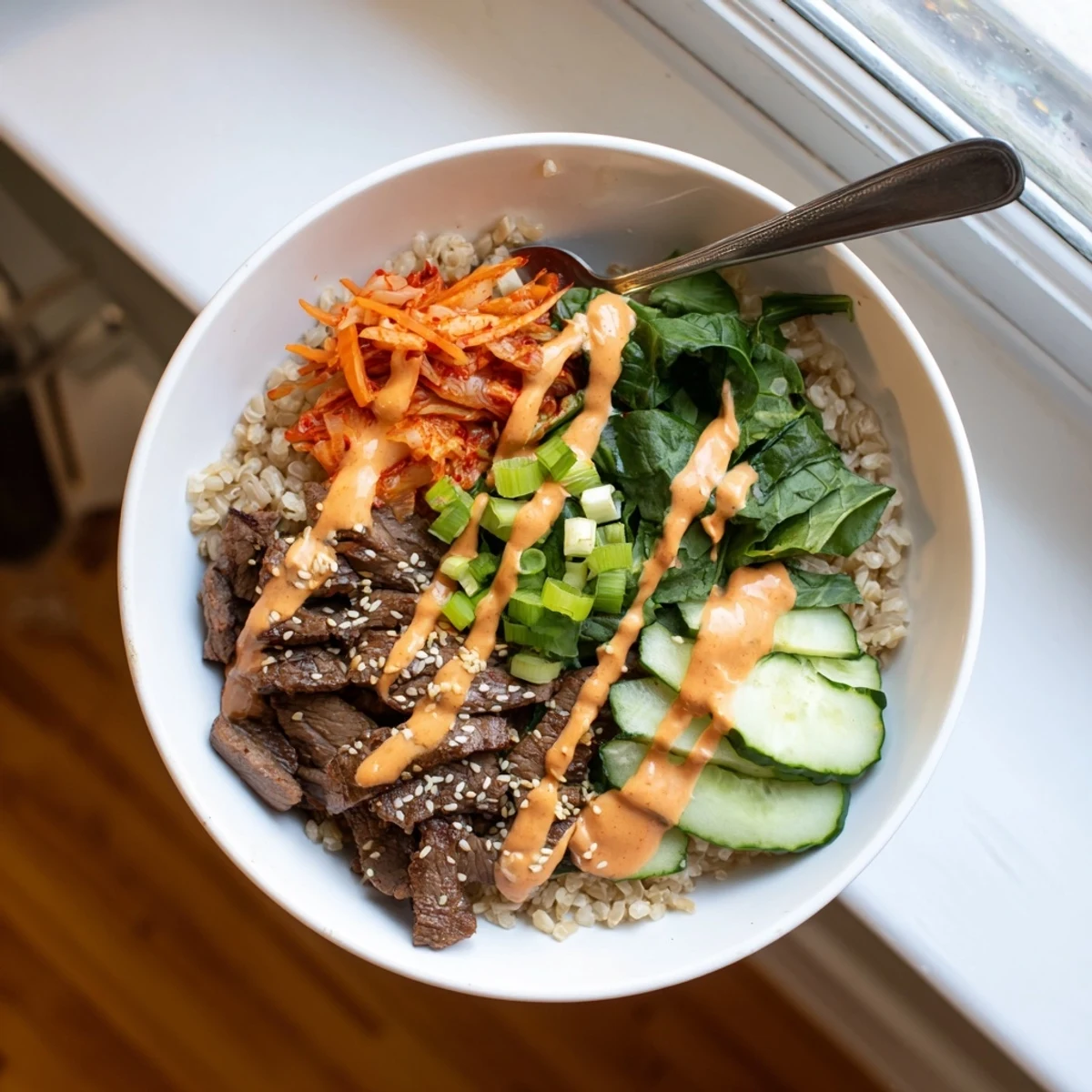 A generous pour of spicy cream sauce finishes Korean BBQ Steak Rice Bowls topped with toasted sesame seeds
