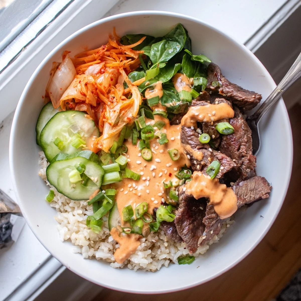 Crisp julienned vegetables and chopped kimchi garnish Korean BBQ Steak Rice Bowls with a bold creamy Sriracha drizzle