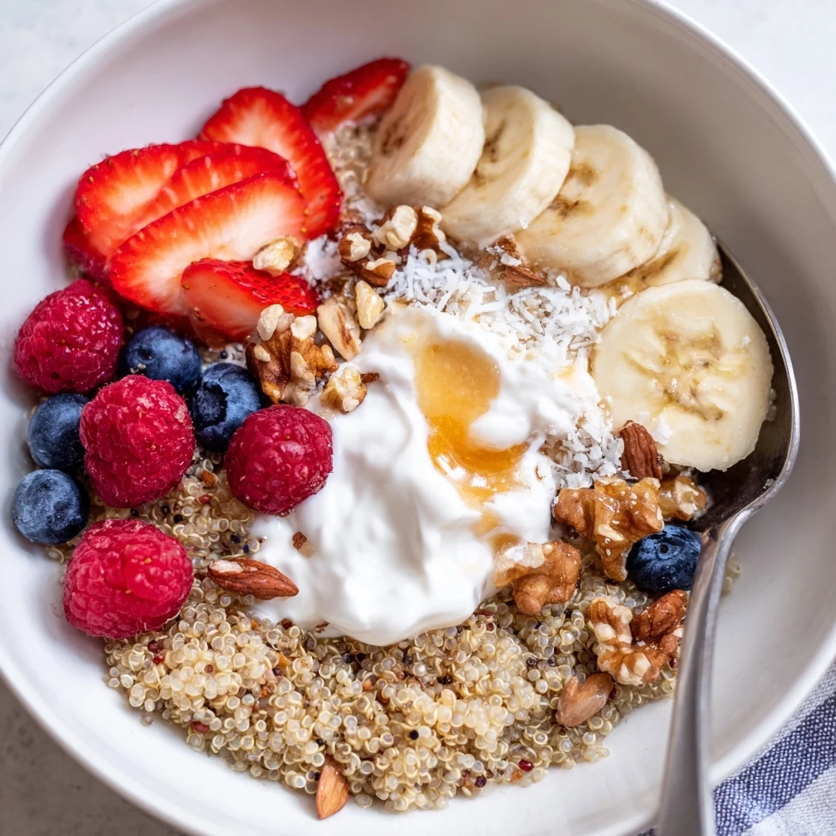 Warm Quinoa Breakfast Bowl topped with sliced banana, crunchy nuts, drizzled honey.