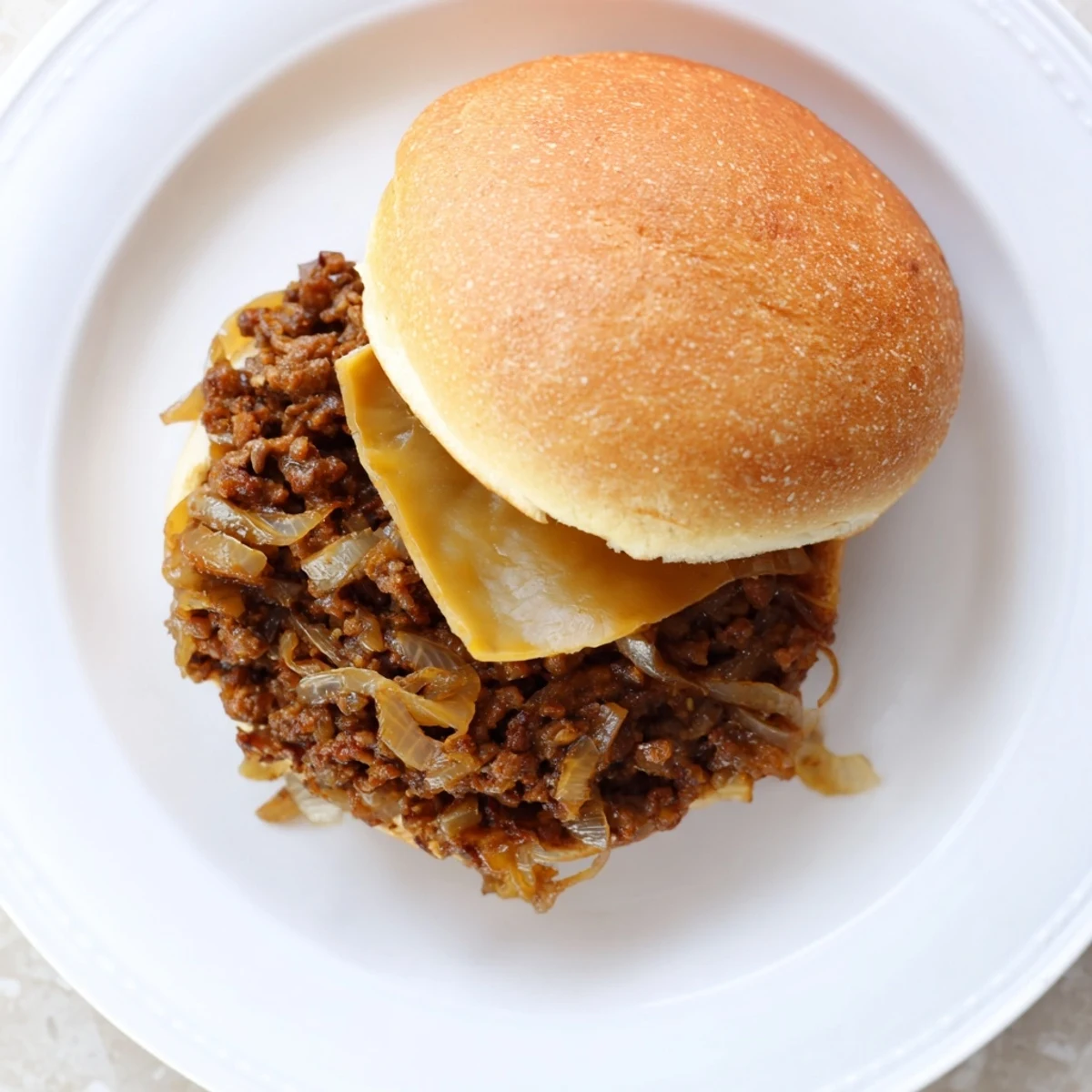 Heaping spoonfuls of rich beef and onion filling overflow from soft French Onion Beef Sloppy Joe sandwiches topped with Swiss