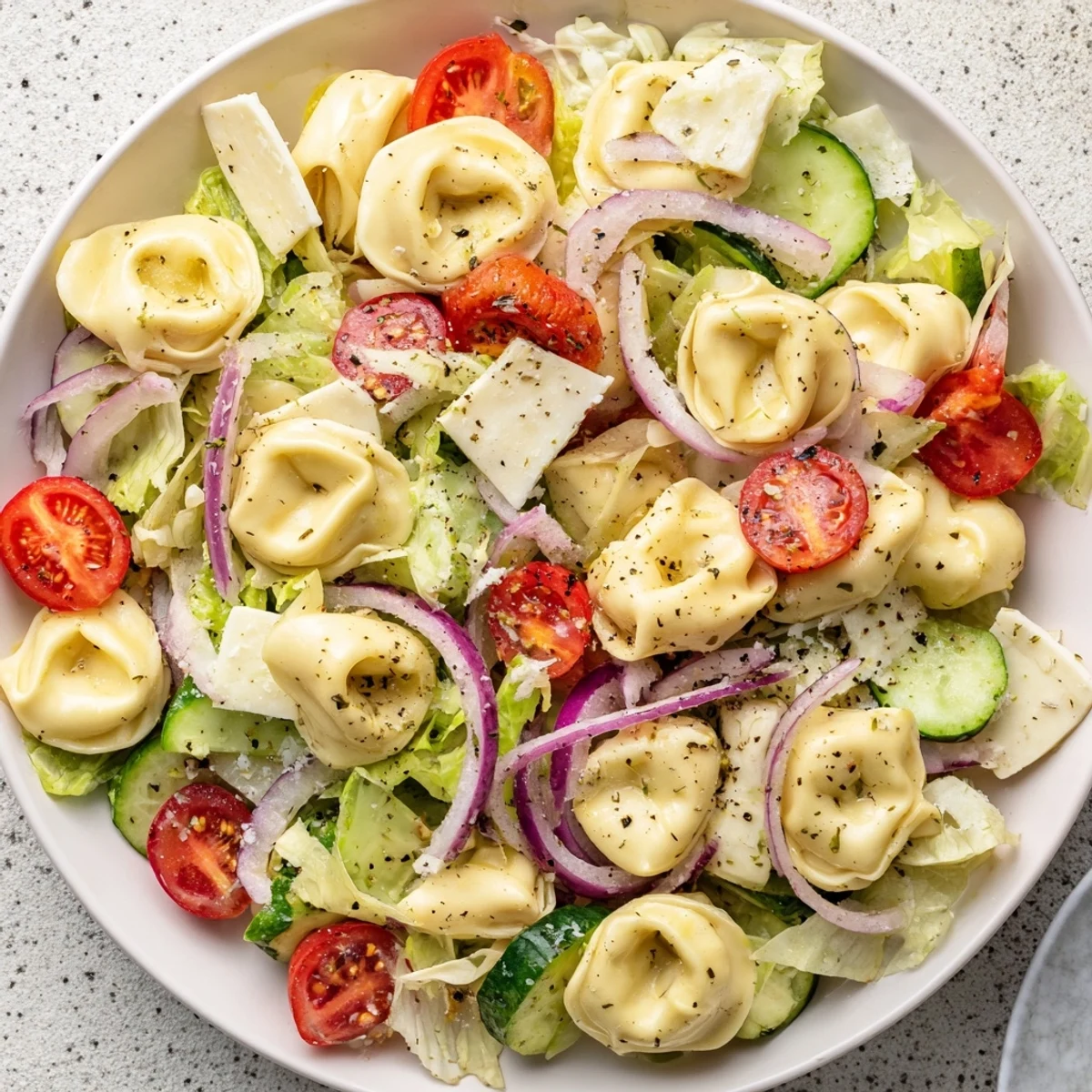 Hearty tortellini salad bowl featuring cherry tomatoes, red peppers, pepperoncini and cubed provolone in oil and vinegar dressing