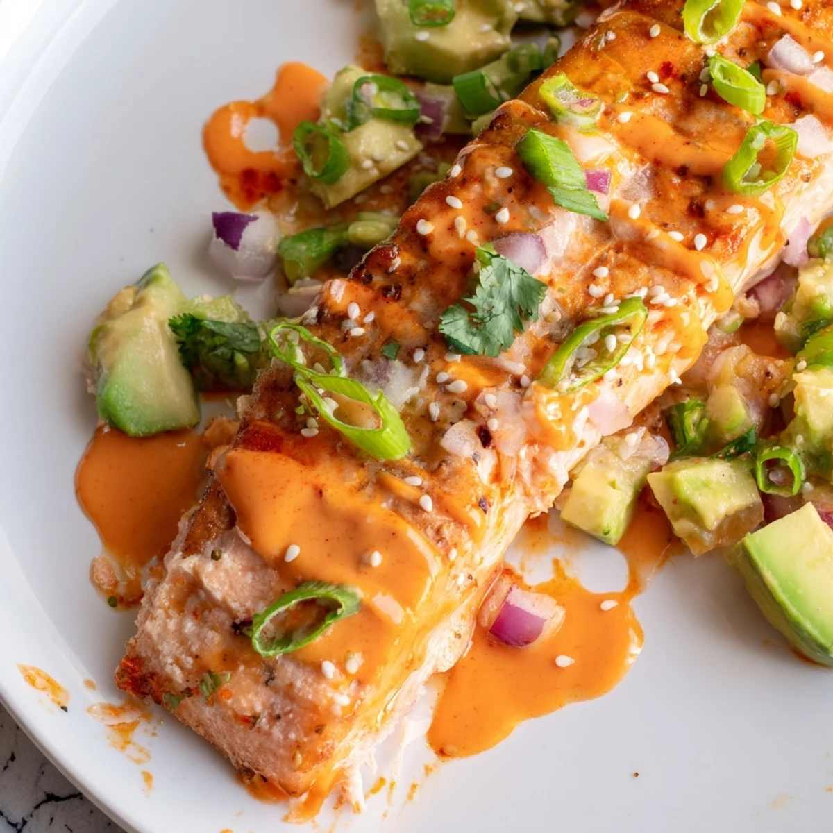 Crispy baked Bang Bang Salmon topped with creamy avocado cucumber salsa on a white plate