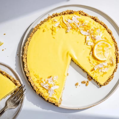No bake vegan lemon tart topped with fresh lemon zest on a nutty almond crust