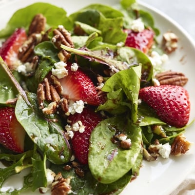 Vibrant Strawberry Fields Salad featuring sweet sliced strawberries, crisp arugula, crumbled goat cheese, and red onion on a white plate